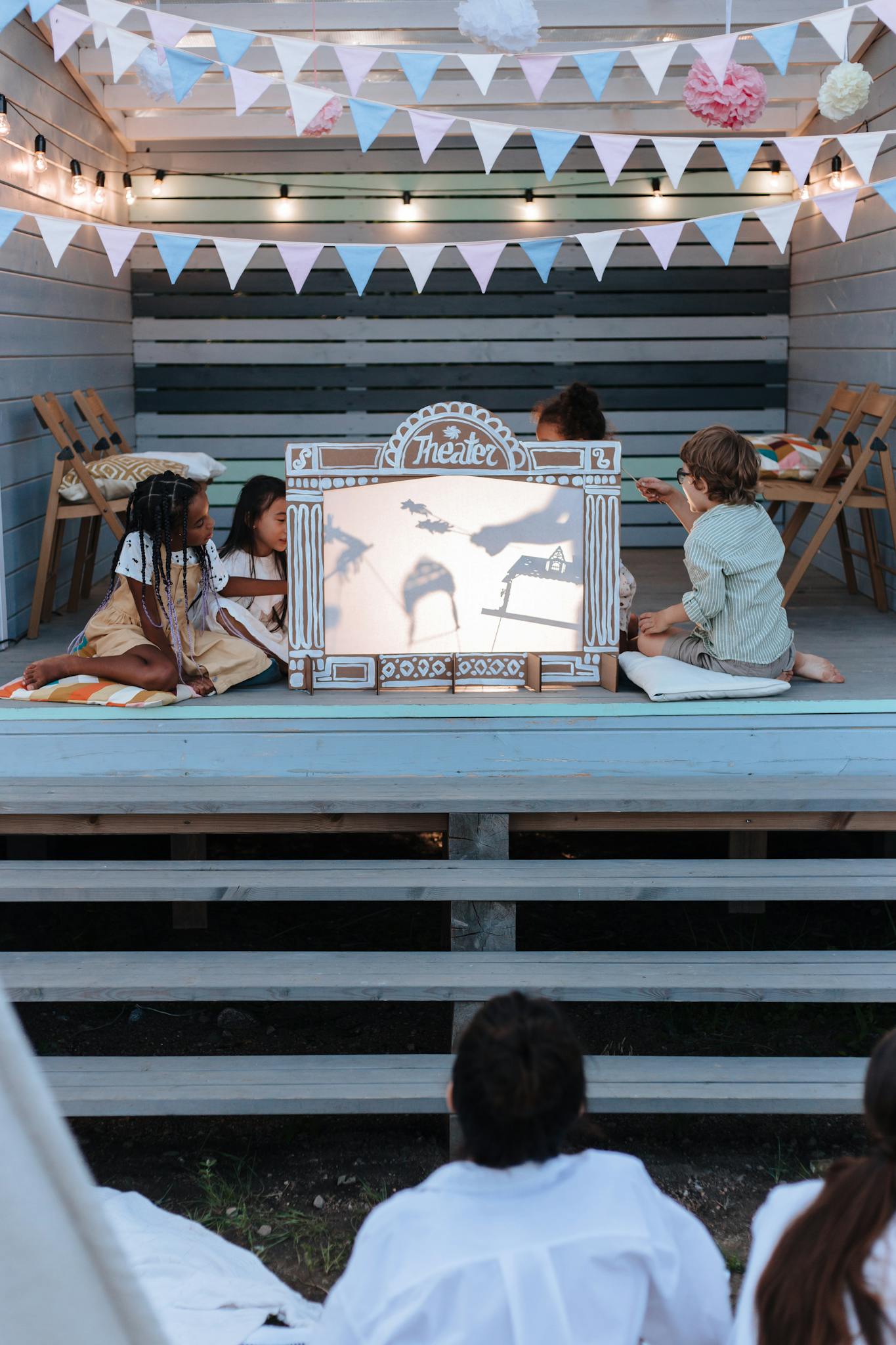 Children engage in a creative puppet show performance on an outdoor stage with bunting decorations.