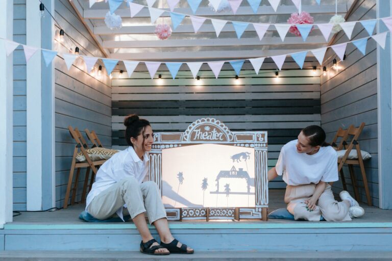 Two women enjoying an outdoor shadow puppet show in a cozy setup.